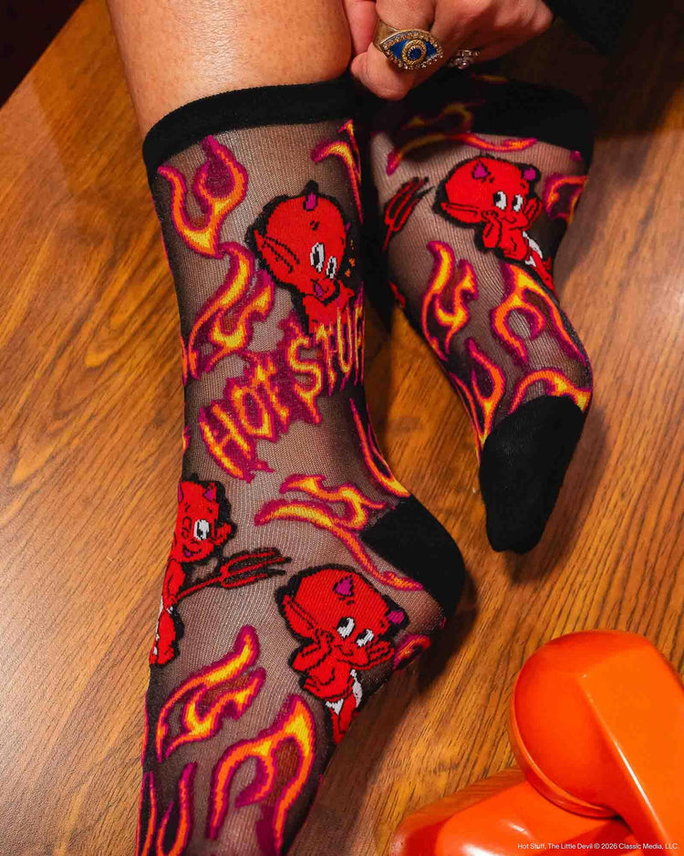 A woman wearing Sock Candy sheer black socks with a red and orange flame and devil graphic pattern.