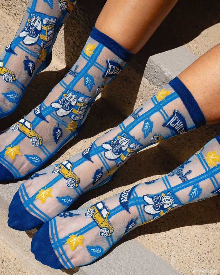 A close up of Sock Candy Gilmore Girls Chilton plaid sheer crew socks featuring a school uniform crest motif.