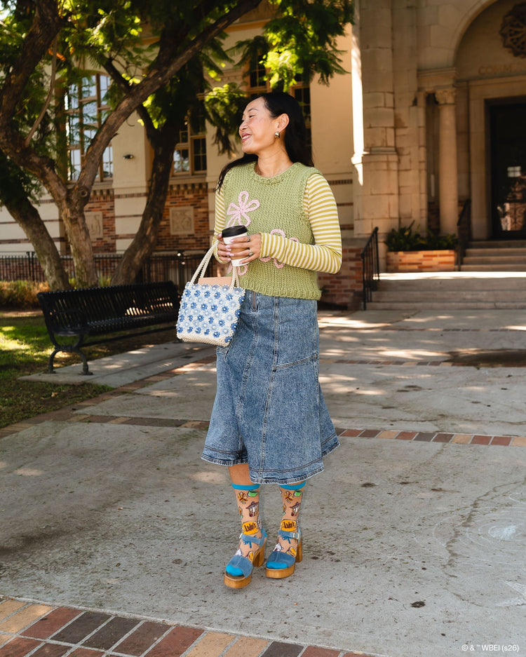 A woman wearing Sock Candy Gilmore Girls Stars Hollow sheer socks with detailed town gazebo and daisy prints, styled with cozy Fall aesthetic clothes and high wooden platform sandals.