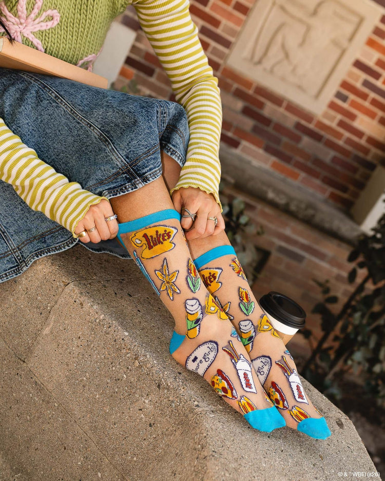A woman wearing Sock Candy Gilmore Girls Stars Hollow sheer socks with detailed town gazebo and daisy prints.
