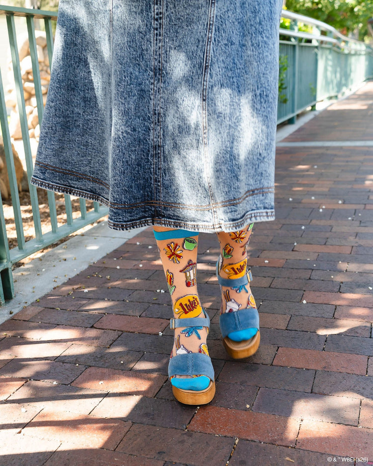 A woman wearing Sock Candy Gilmore Girls Stars Hollow sheer socks with detailed town gazebo and daisy prints, styled with high wooden platform sandals.