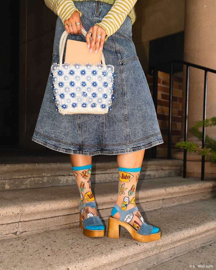 A woman wearing Sock Candy Gilmore Girls Stars Hollow sheer socks with detailed town gazebo and daisy prints, styled with high wooden platform sandals.