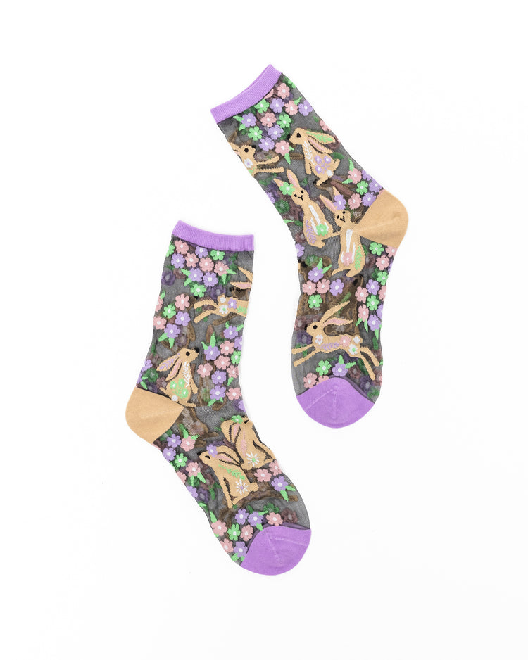 A pair of black sheer Sock Candy socks with a rabbit and floral design on a white background.
