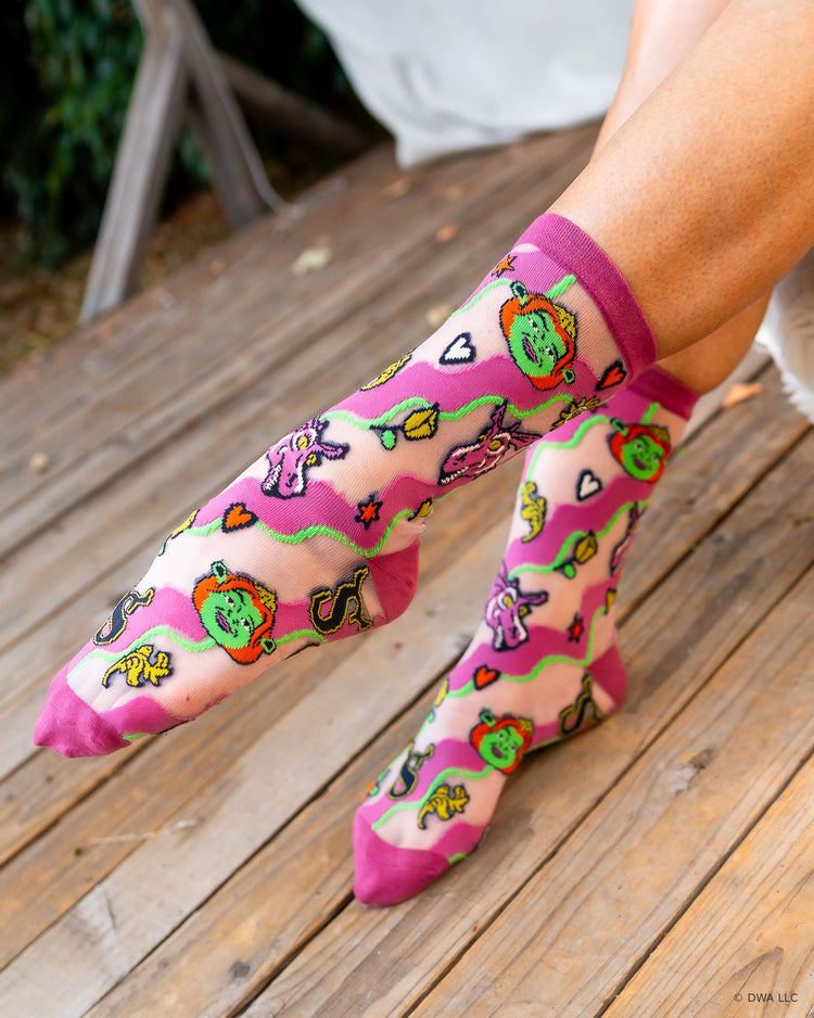 A pair of sheer Shrek socks designed by Sock Candy, worn on a woman's feet on a wooden stage.